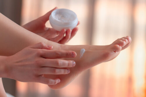 Woman caring about her feet and applying hydrating, moisturizing cream. Foot and skin care